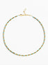A delicate gold chain necklace with small, evenly spaced light blue beads, displayed in a circular shape against a clean white background.