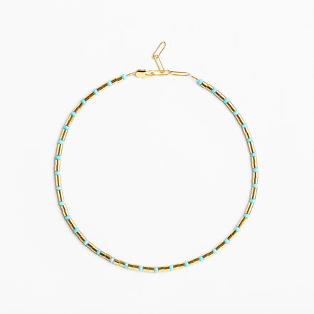 A delicate gold chain necklace with small, evenly spaced light blue beads, displayed in a circular shape against a clean white background.