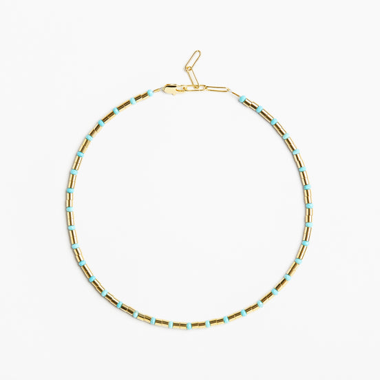 A delicate gold chain necklace with small, evenly spaced light blue beads, displayed in a circular shape against a clean white background.