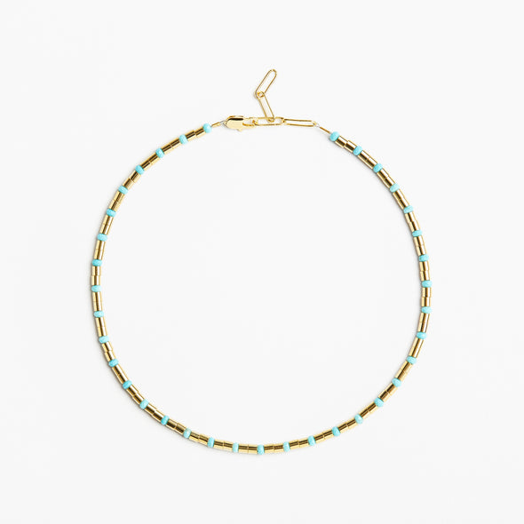 A delicate gold chain necklace with small, evenly spaced light blue beads, displayed in a circular shape against a clean white background.
