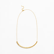 A delicate gold chain necklace featuring a textured, curved bar pendant at the bottom, displayed against a clean white background.