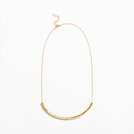 A delicate gold chain necklace featuring a textured, curved bar pendant at the bottom, displayed against a clean white background.