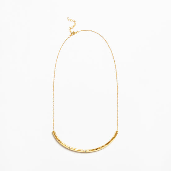 A delicate gold chain necklace featuring a textured, curved bar pendant at the bottom, displayed against a clean white background.