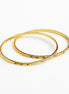 Two thin gold bangles with small dark green stone accents, overlapping on a plain white background.
