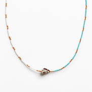 A delicate beaded necklace featuring turquoise blue and white beads with small orange accents, centered with a natural cowrie shell pendant on a clean white background.