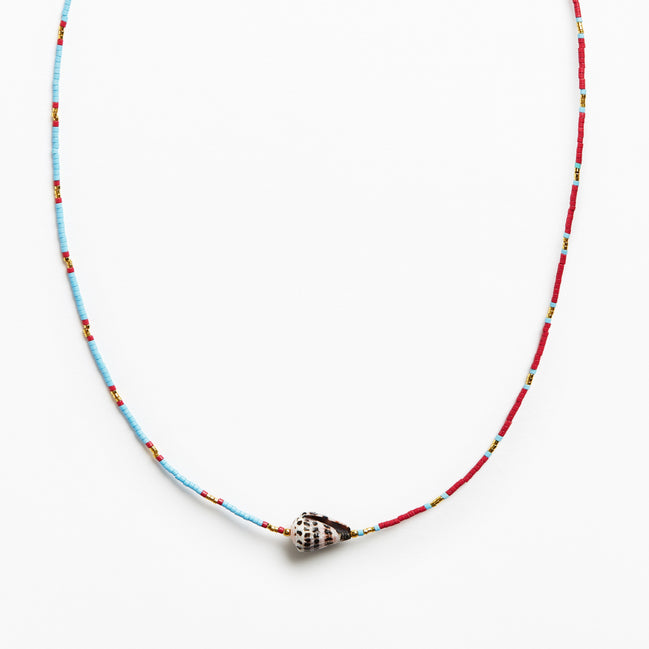 A beaded necklace featuring a light blue and red string with small yellow accents, finished with a silver conch shell pendant, shown against a plain white background.