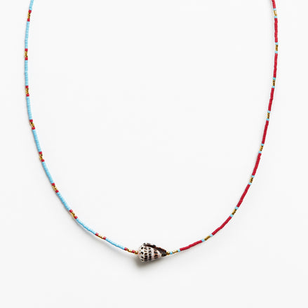 A beaded necklace featuring a light blue and red string with small yellow accents, finished with a silver conch shell pendant, shown against a plain white background.