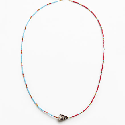 A delicate beaded necklace with alternating light blue and red beads, featuring a small metallic shell-shaped charm at the center, displayed on a clean white background.
