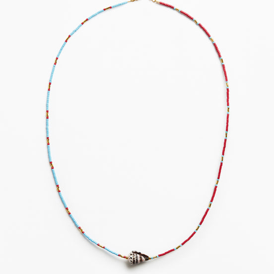 A delicate beaded necklace with alternating light blue and red beads, featuring a small metallic shell-shaped charm at the center, displayed on a clean white background.