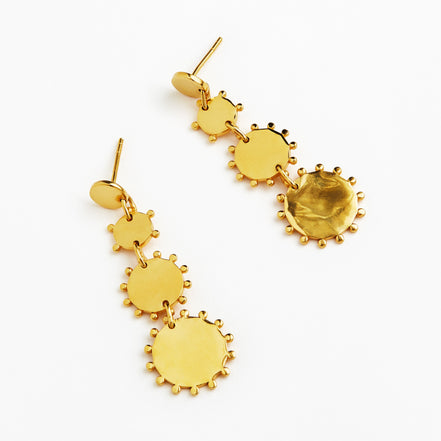 A pair of gold dangle earrings with a series of textured circular disc charms of varying sizes, shown on a plain white background.