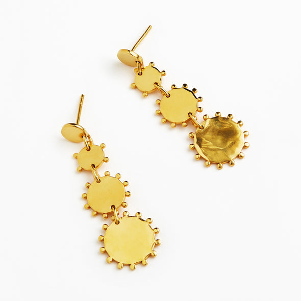 A pair of gold dangle earrings with a series of textured circular disc charms of varying sizes, shown on a plain white background.