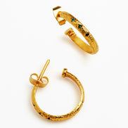 A pair of textured gold hoop earrings with small green and blue gemstone accents, displayed on a clean white background.