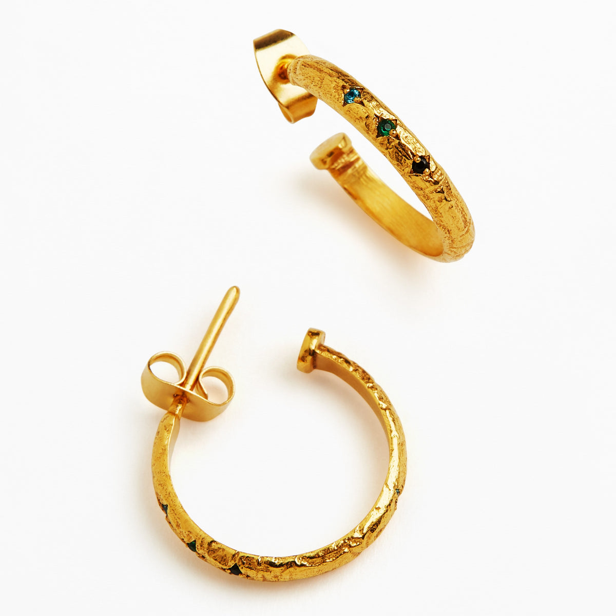 A pair of textured gold hoop earrings with small green and blue gemstone accents, displayed on a clean white background.