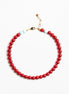 A beaded necklace featuring a continuous strand of glossy red beads, accented by two small light blue beads and a gold-tone lobster clasp, displayed on a clean white background.