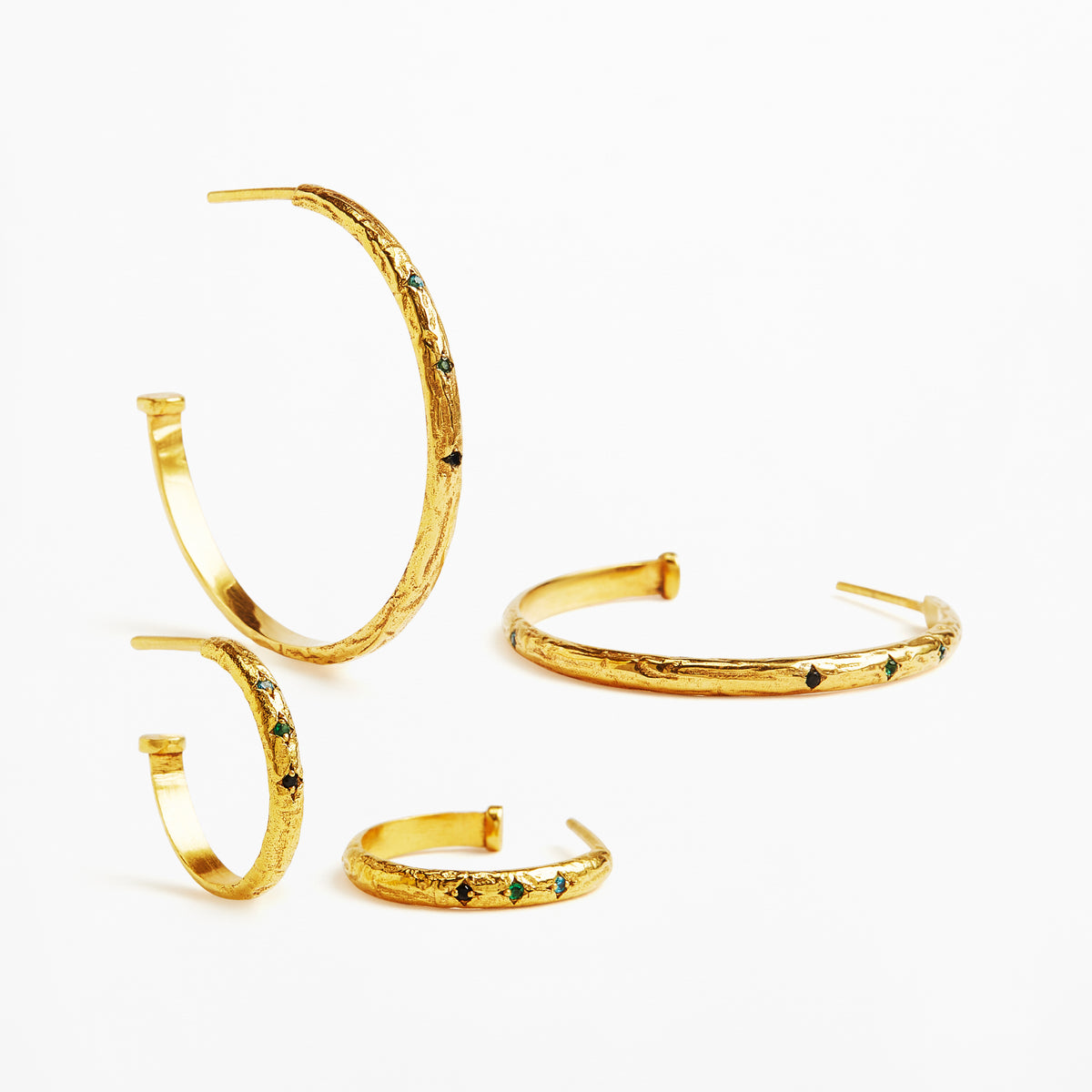Four textured gold hoop and cuff earrings with small green and black stone accents, arranged on a clean white background.