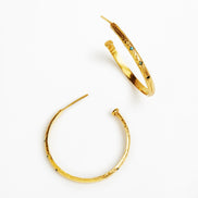 A pair of textured gold hoop earrings with small dark and light blue gemstone accents, displayed on a clean white background.