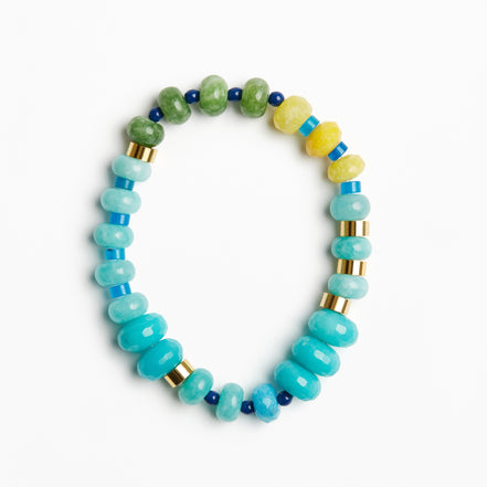 A beaded stretch bracelet featuring light blue and turquoise beads, green and yellow stone beads, and small gold spacer rings, displayed on a clean white background.