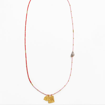 A delicate beaded necklace featuring a red and light pink string with small metallic beads, a silver-toned bell-shaped charm, and two gold-toned pendant tags at the bottom, displayed on a clean white background.