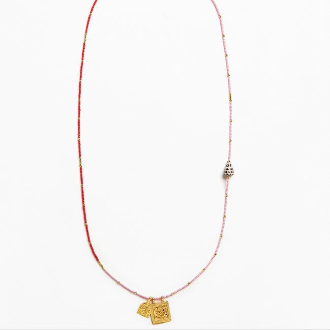 A delicate beaded necklace featuring a red and light pink string with small metallic beads, a silver-toned bell-shaped charm, and two gold-toned pendant tags at the bottom, displayed on a clean white background.
