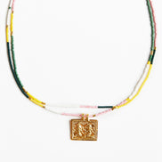 A beaded necklace featuring a central gold-toned square pendant with an embossed design, suspended over strands of small beads in green, yellow, white, and light pink on a plain white background.