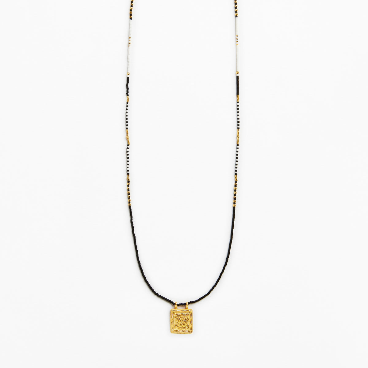 A long beaded necklace featuring a black cord, white and black beads, and a small gold square pendant with an engraved design, shown against a plain white background.