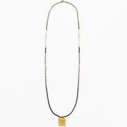 A long beaded necklace featuring a black cord base, accented with small white and gold beads, and finished with a square gold pendant at the bottom, shown against a plain white background.