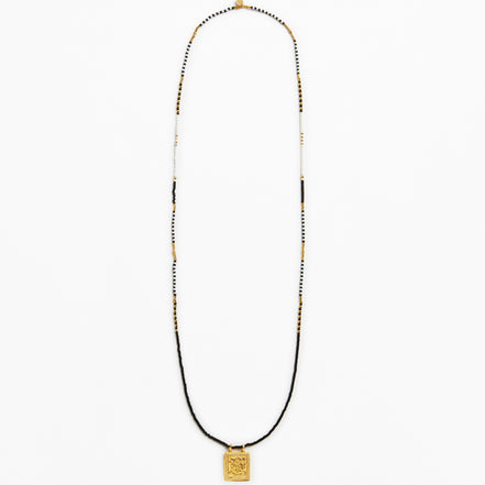A long beaded necklace featuring a black cord base, accented with small white and gold beads, and finished with a square gold pendant at the bottom, shown against a plain white background.