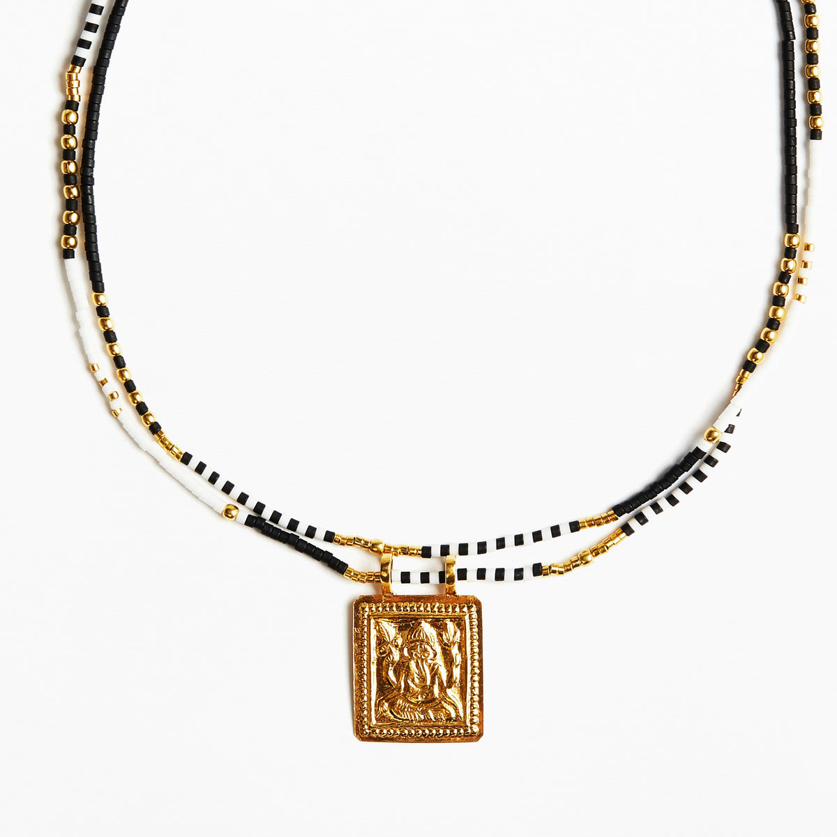 A beaded necklace featuring black and white beads with gold-toned chain accents and a square gold pendant with an embossed figure, shown against a plain white background.