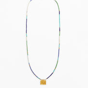 A long beaded necklace with a textured gold square pendant, featuring beads in blue, green, white, and gold.