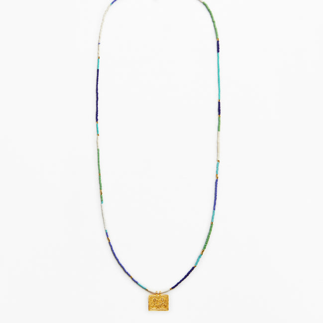 A long beaded necklace with a textured gold square pendant, featuring beads in blue, green, white, and gold.