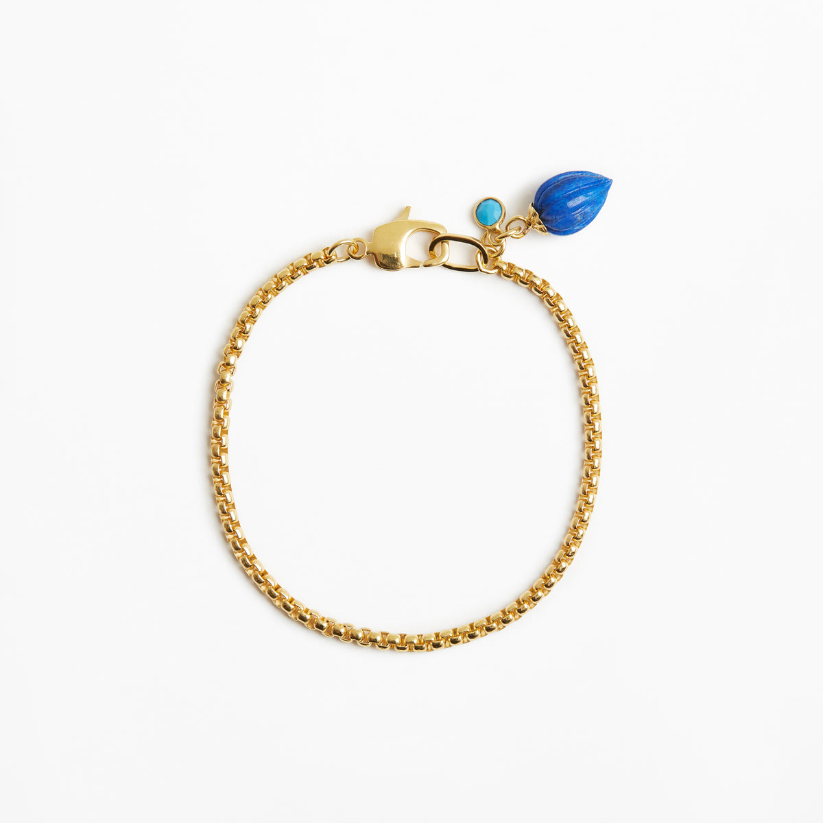 A gold chain bracelet with a lobster clasp, a small turquoise bead, and a larger blue teardrop charm, displayed on a clean white background.