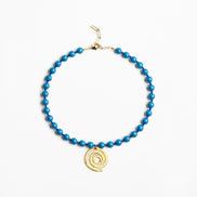A beaded necklace featuring bright blue beads and a gold spiral pendant, displayed on a clean white background.