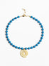 A beaded necklace featuring bright blue beads and a gold spiral pendant, displayed on a clean white background.