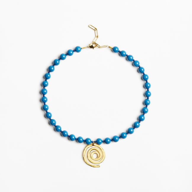 A beaded necklace featuring bright blue beads and a gold spiral pendant, displayed on a clean white background.