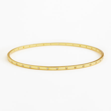 A thin gold bangle bracelet with small clear rhinestones set along the front edge, displayed on a clean white background.