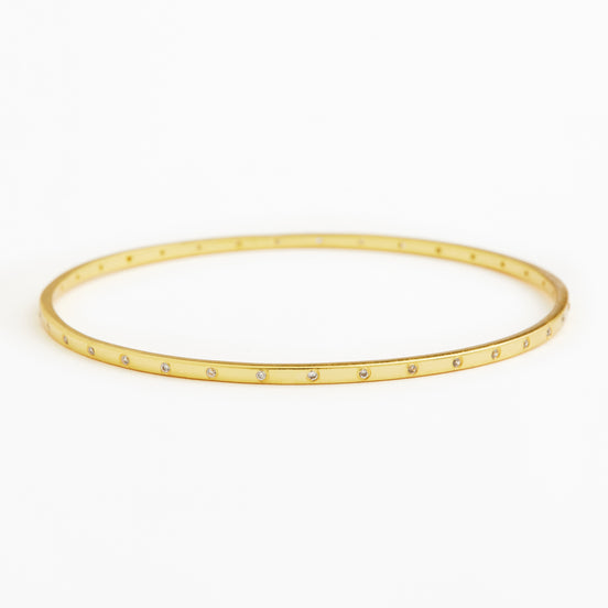 A thin gold bangle bracelet with small clear rhinestones set along the front edge, displayed on a clean white background.