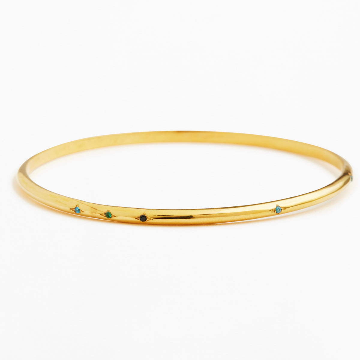 A thin yellow gold bangle bracelet with five small, evenly spaced colored gemstone accents in blue, green, and black, set against a plain white background.
