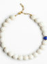 A beaded necklace with matte white round beads, a single small blue bead accent, and gold-tone metal hardware, photographed on a clean white background.