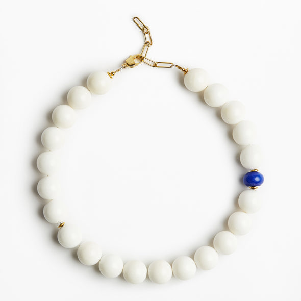 A beaded necklace with matte white round beads, a single small blue bead accent, and gold-tone metal hardware, photographed on a clean white background.
