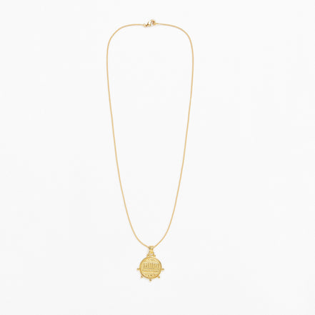A delicate gold chain necklace with a small round ship's wheel pendant, displayed against a clean white background.