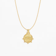 A gold pendant necklace featuring a circular coin-style charm with an engraved arch design, suspended from a delicate gold chain against a plain white background.