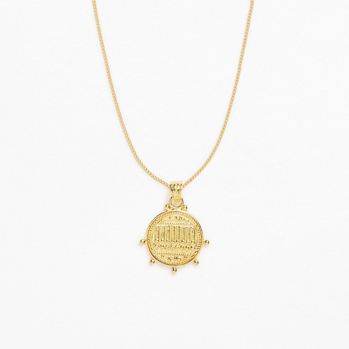 A gold pendant necklace featuring a circular coin-style charm with an engraved arch design, suspended from a delicate gold chain against a plain white background.