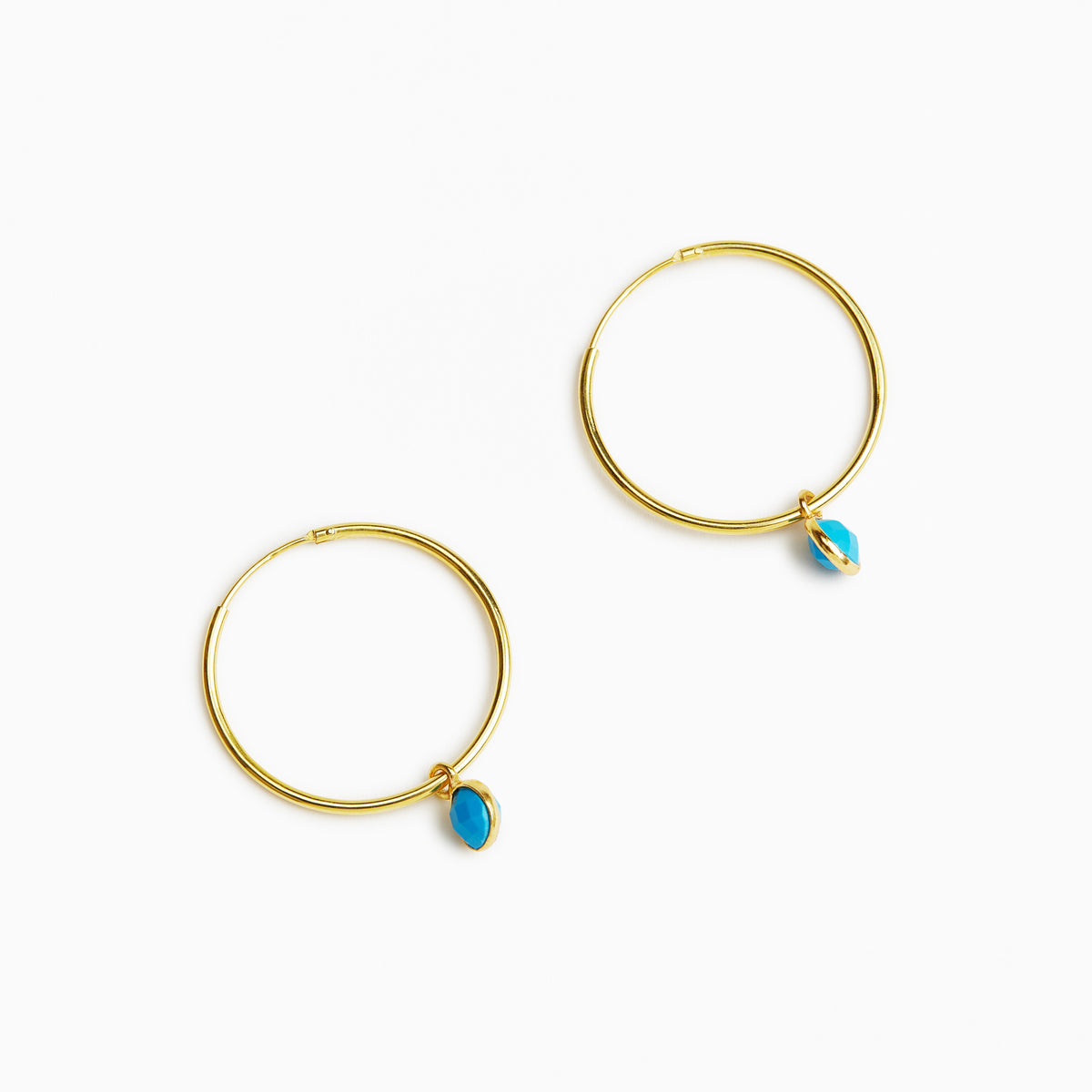 A pair of gold hoop earrings, each adorned with a small teardrop-shaped turquoise stone, displayed on a clean white background.