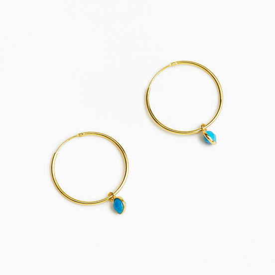 A pair of gold hoop earrings, each adorned with a small teardrop-shaped turquoise stone, displayed on a clean white background.