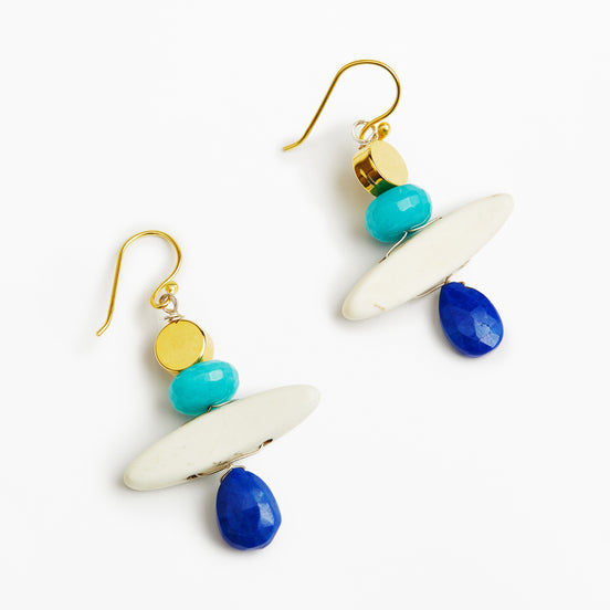 A pair of bohemian dangle earrings featuring gold-tone fishhook wires, white oval beads, turquoise and gold round beads, and faceted blue teardrop beads, displayed on a clean white background.