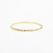A thin gold bangle bracelet with a textured, hammered finish and small dark green stone accents spaced along the front edge, shown on a plain white background.