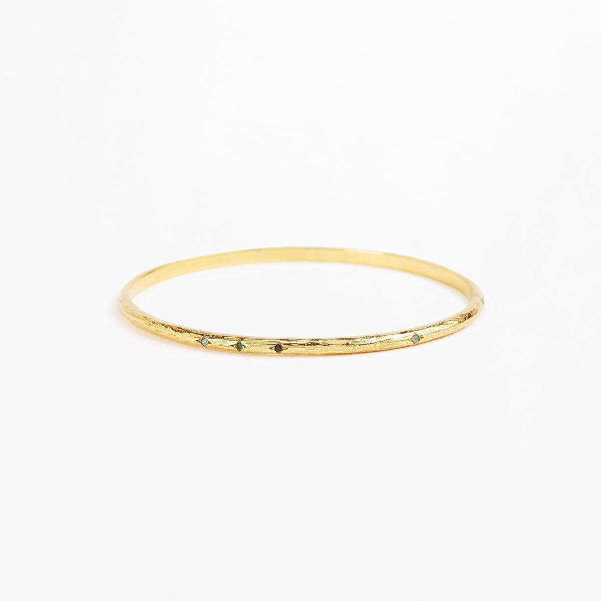A thin gold bangle bracelet with a textured, hammered finish and small dark green stone accents spaced along the front edge, shown on a plain white background.