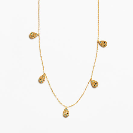 A delicate gold chain necklace featuring five small teardrop-shaped pendants, each decorated with tiny black and yellow inlay details, set against a plain white background.