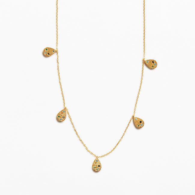 A delicate gold chain necklace featuring five small teardrop-shaped pendants, each decorated with tiny black and yellow inlay details, set against a plain white background.