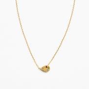 A delicate gold chain necklace featuring a small teardrop-shaped pendant adorned with tiny green and blue stones and a central black detail, set against a plain white background.